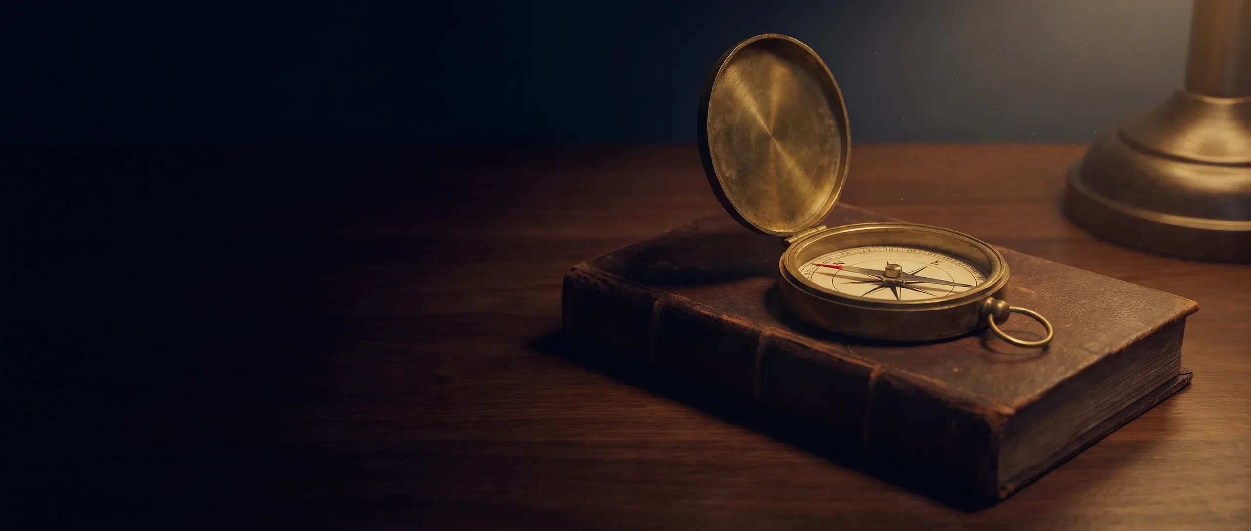 An open brass compass resting on a leather-bound book on a dark desk.